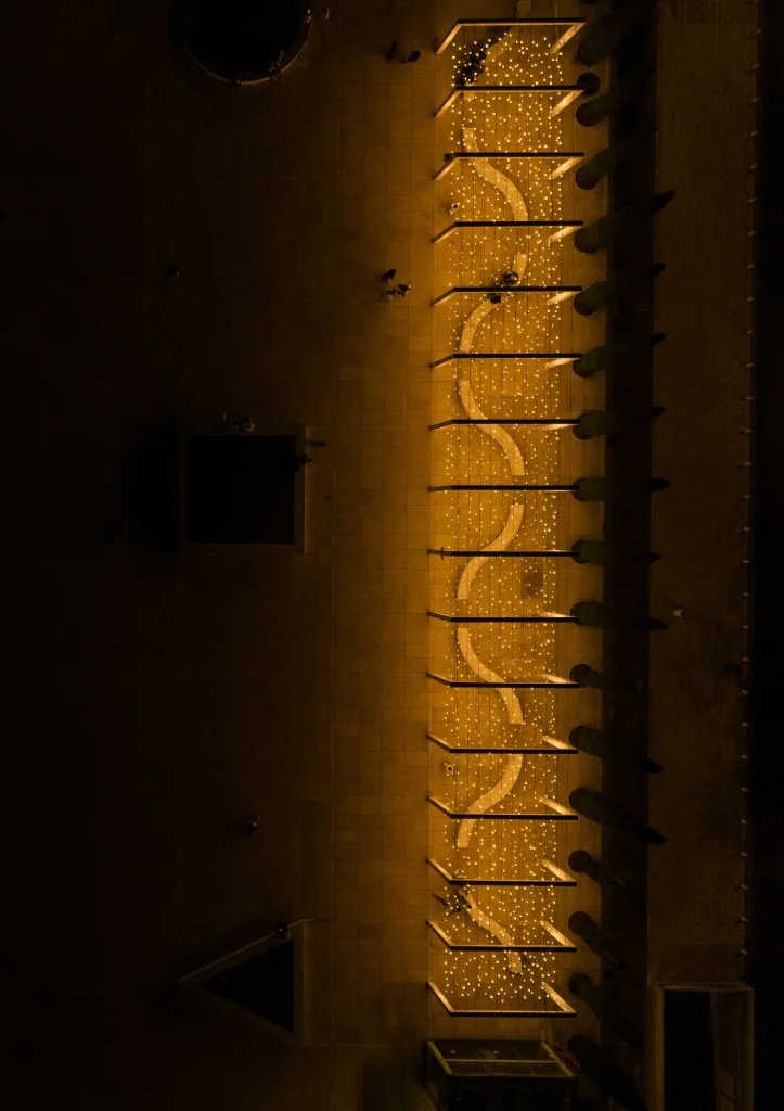 Aerial night view of the Light Monument from above, showing thousands of warm lights in a long rectangular field with a winding central path