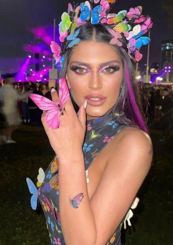 Kim Dukarker at an outdoor nighttime event with butterfly-themed headpiece, makeup, ring, and tattoo
