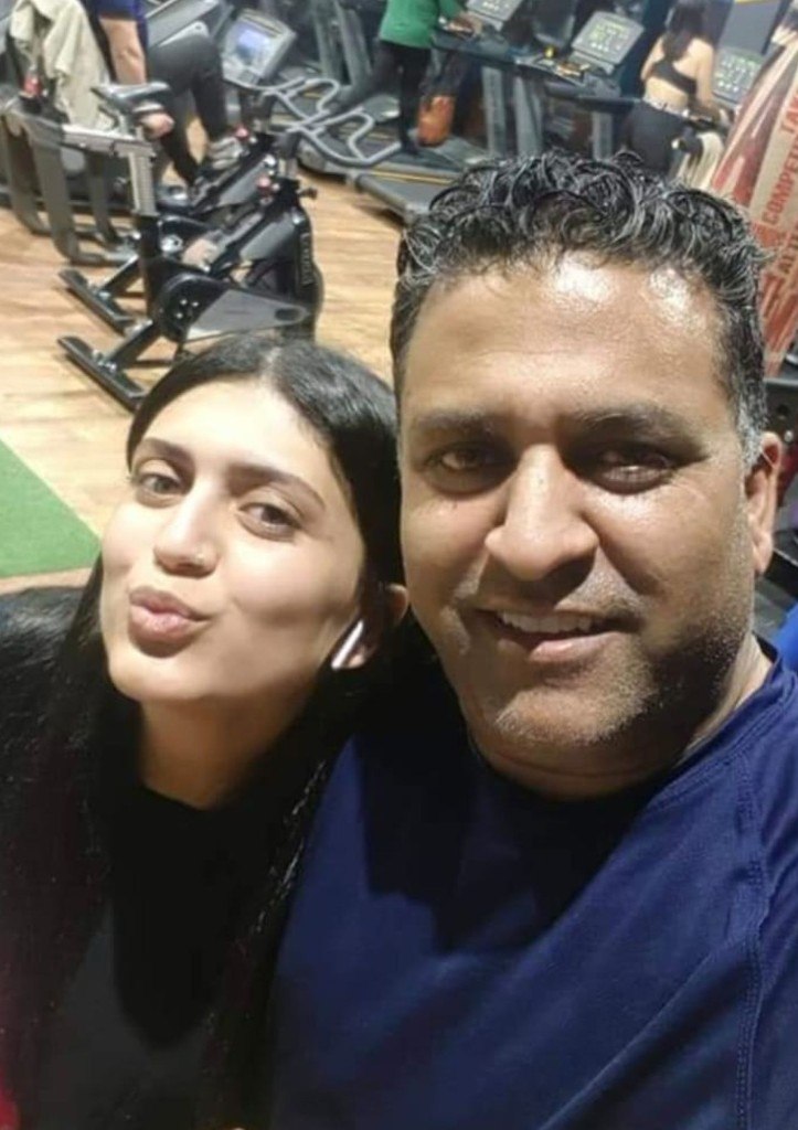 A playful gym selfie of Kim with earbuds and a man smiling beside her